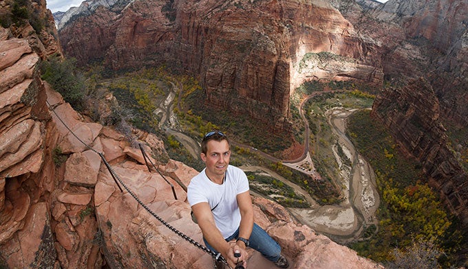 Zion-Angels-Landing-chains-hiker_Dollar_680 A hiker near the top of Angels Landing in Zion National Park, holding onto the chains and taking a selfie photo.